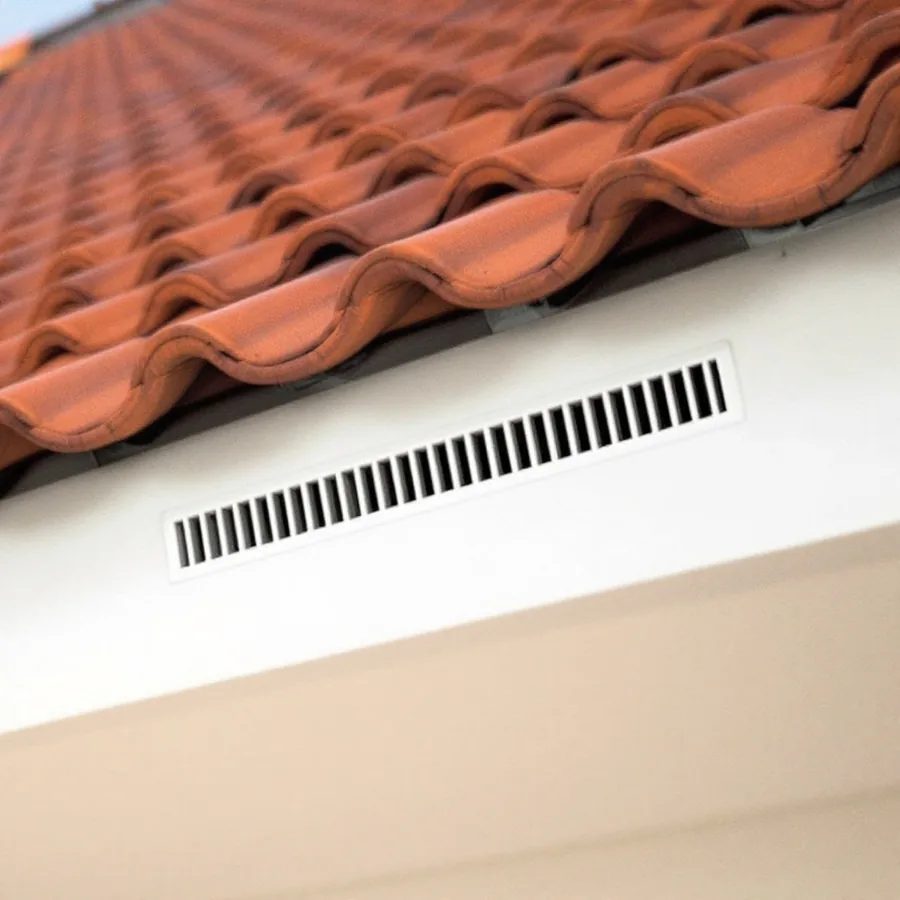 The eave of a tile roof seen from below, showing the underside of the tiles, the fascia board and a continuous slotted soffit vent running along it