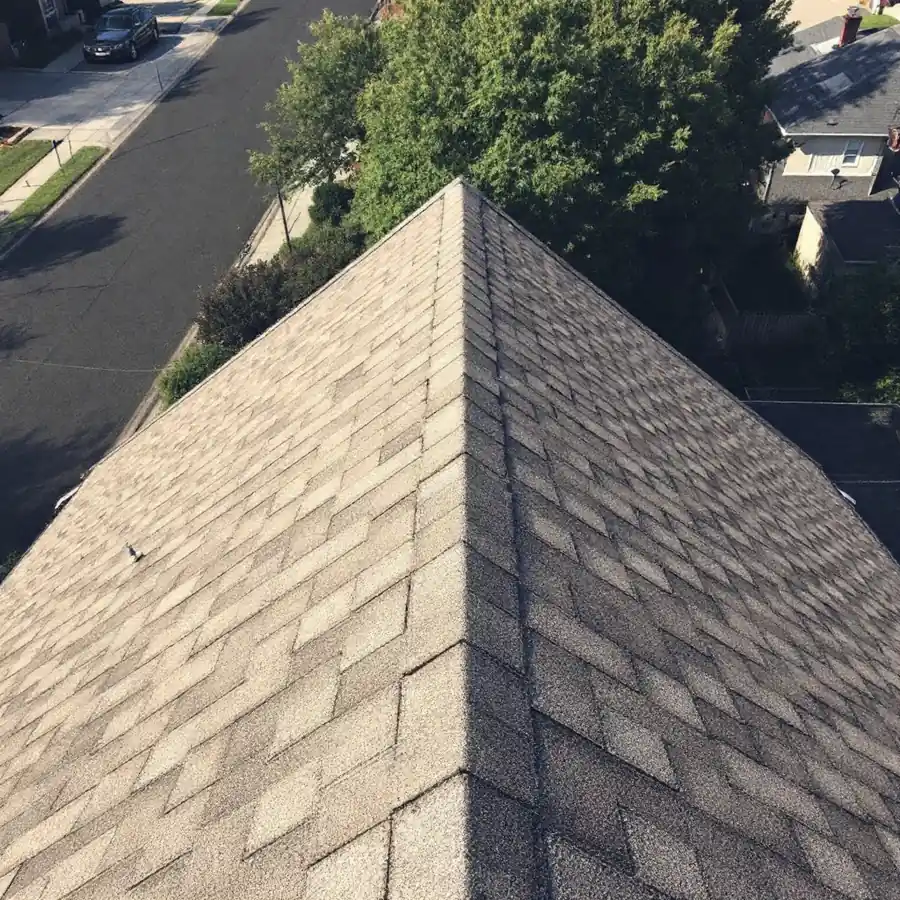 Looking down the hip of a shingle roof from above, the slope on the left noticeably paler and washed out while the slope on the right stays dark
