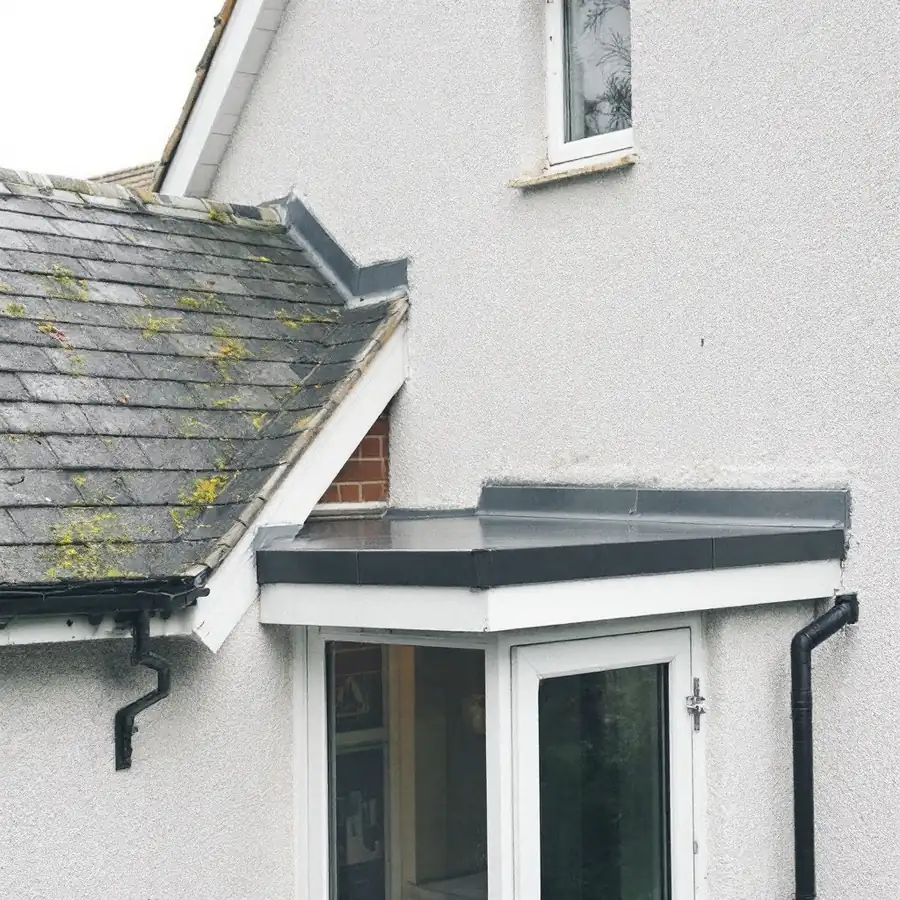 House where a small flat roof over a porch meets the pitched main roof and a wall, showing the junction