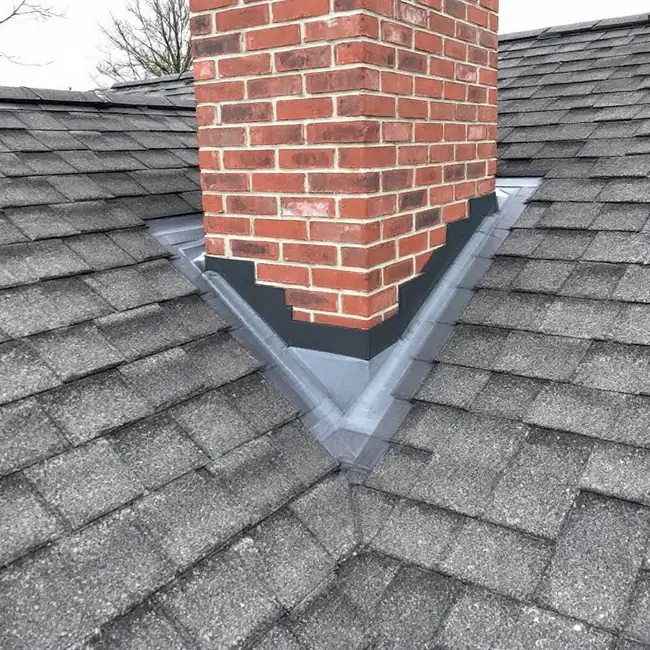 Brick chimney rising through an asphalt shingle roof with step flashing and counter-flashing visible along both sides