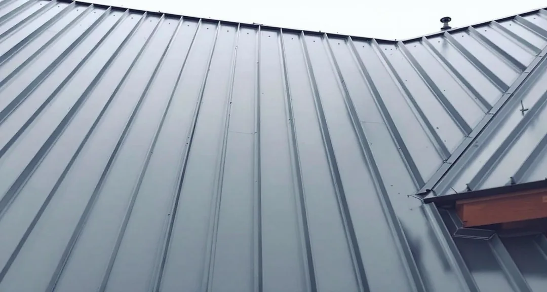 Dark gray standing seam metal roof photographed from below, raised interlocking seams running from ridge to eave with no fasteners visible on the panel surface