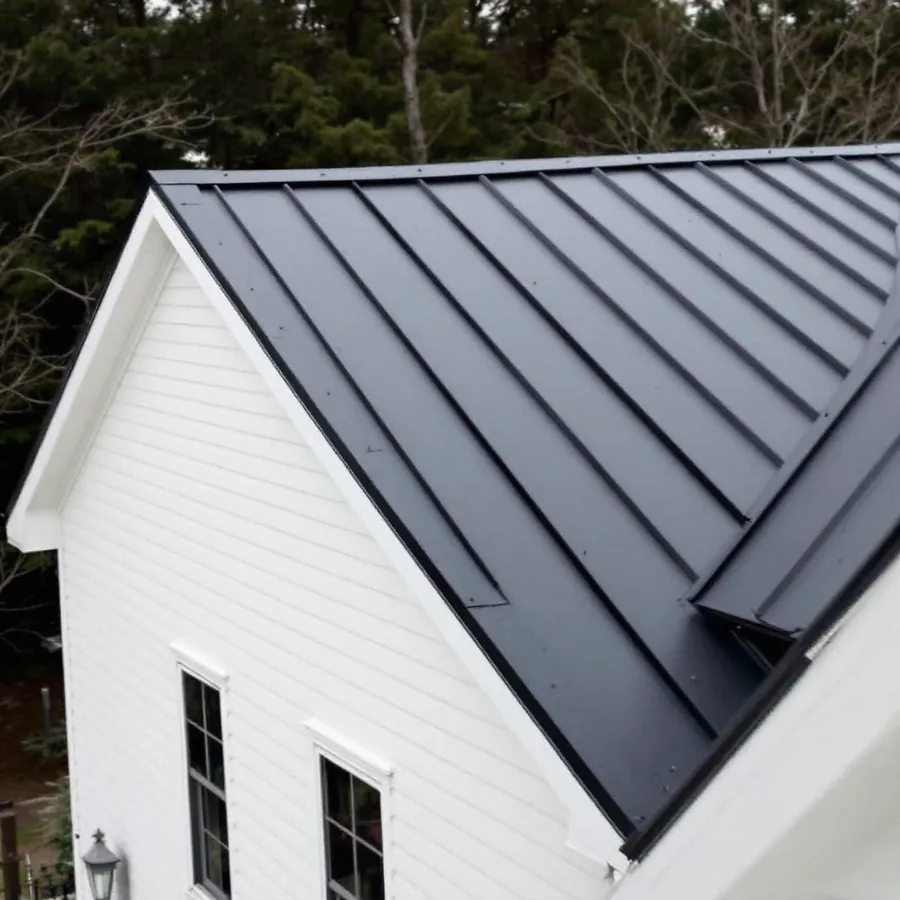 A residential roof in near-black matte standing seam metal against pale siding