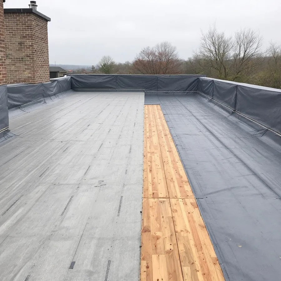 Bare roof deck half covered with gray synthetic underlayment rolled out and fastened, the other half still bare wood